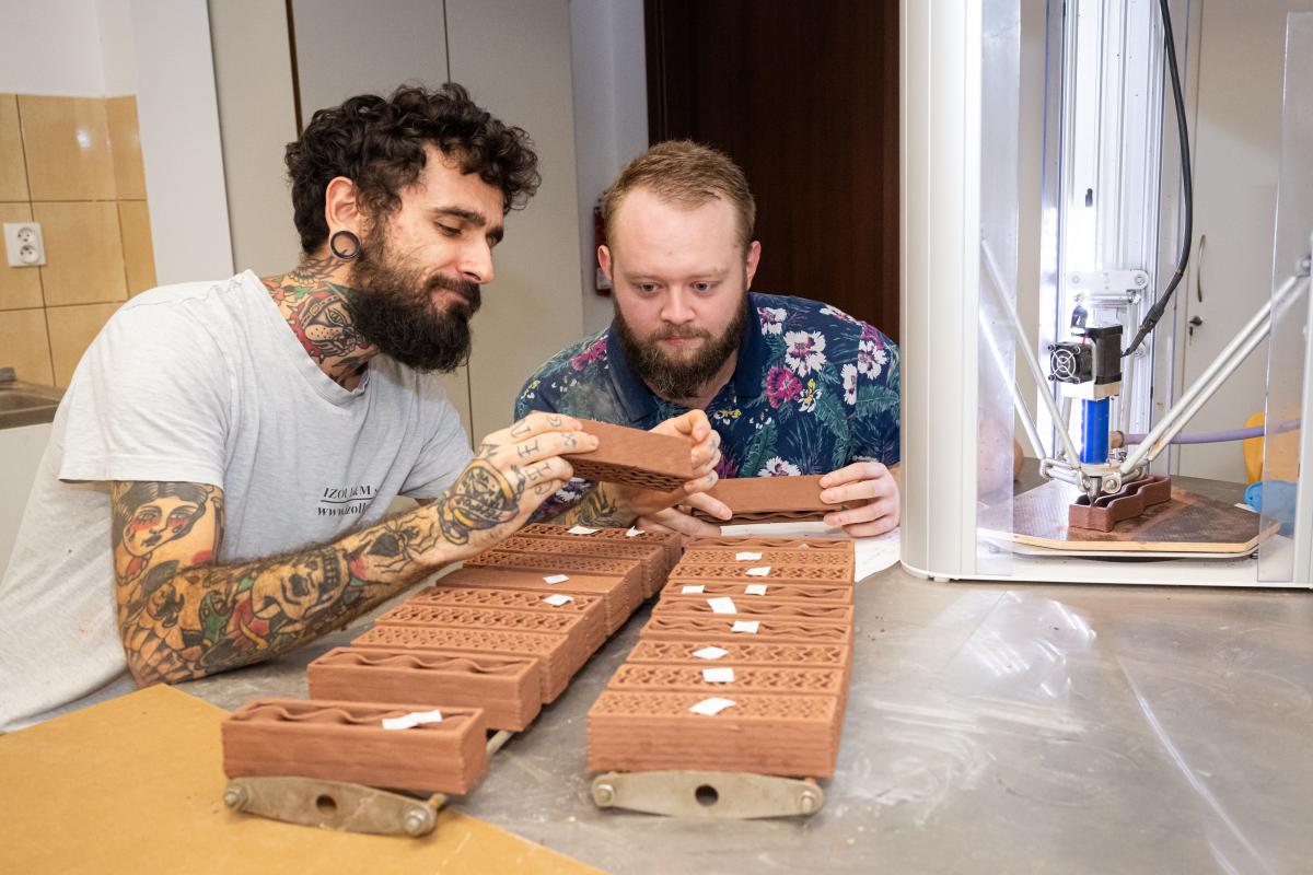 dwwóch doktorantó z Uniwersytetu w Ostrawie Ing. Radoslav Gandel oraz Ing. Jan Jeřábek. patrzą na wydrukowane elenenty na drukawce 3D. zdjęcie zrobione w laborairium z kierunku budownictwo.